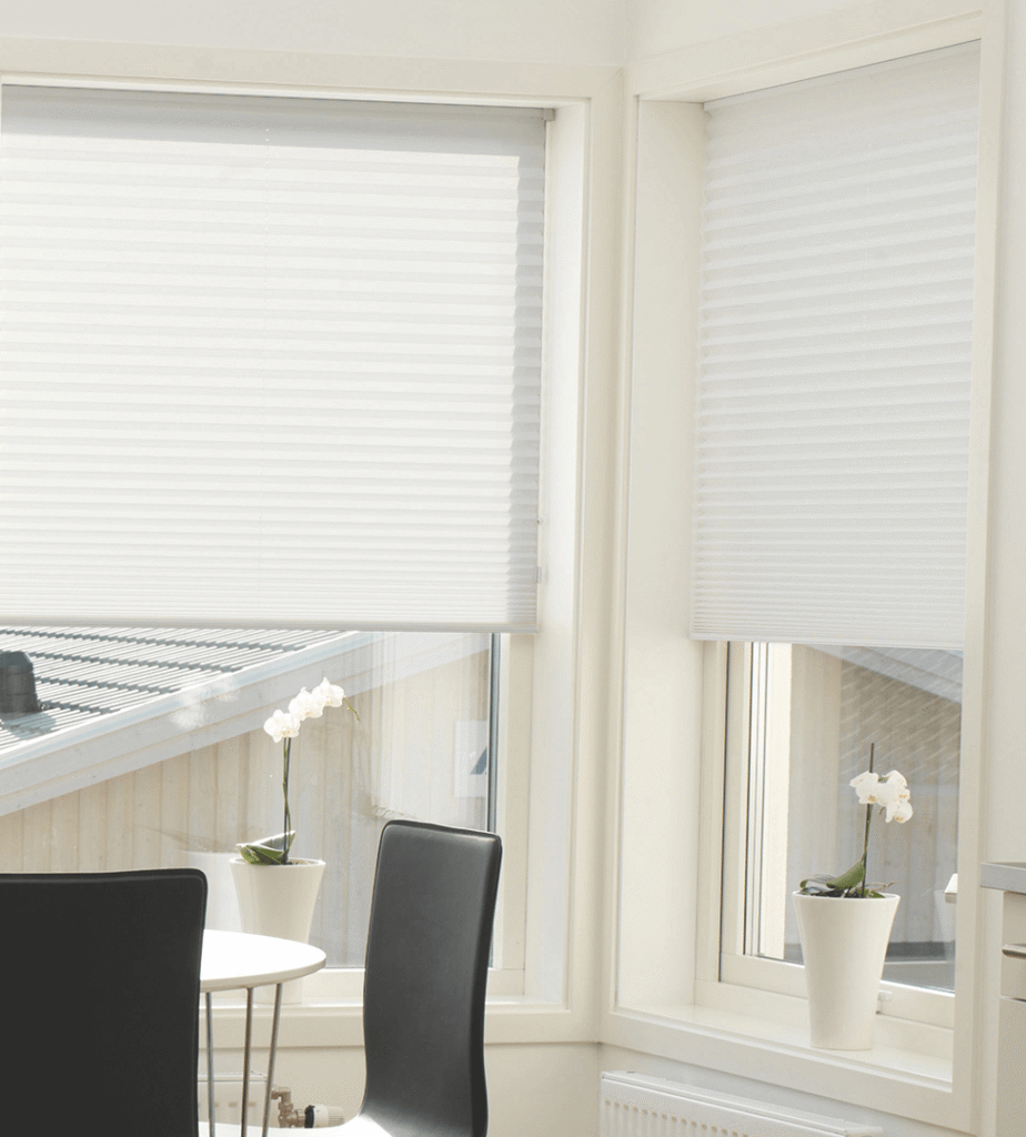 Hvide plisségardiner i en lyse spisestue.