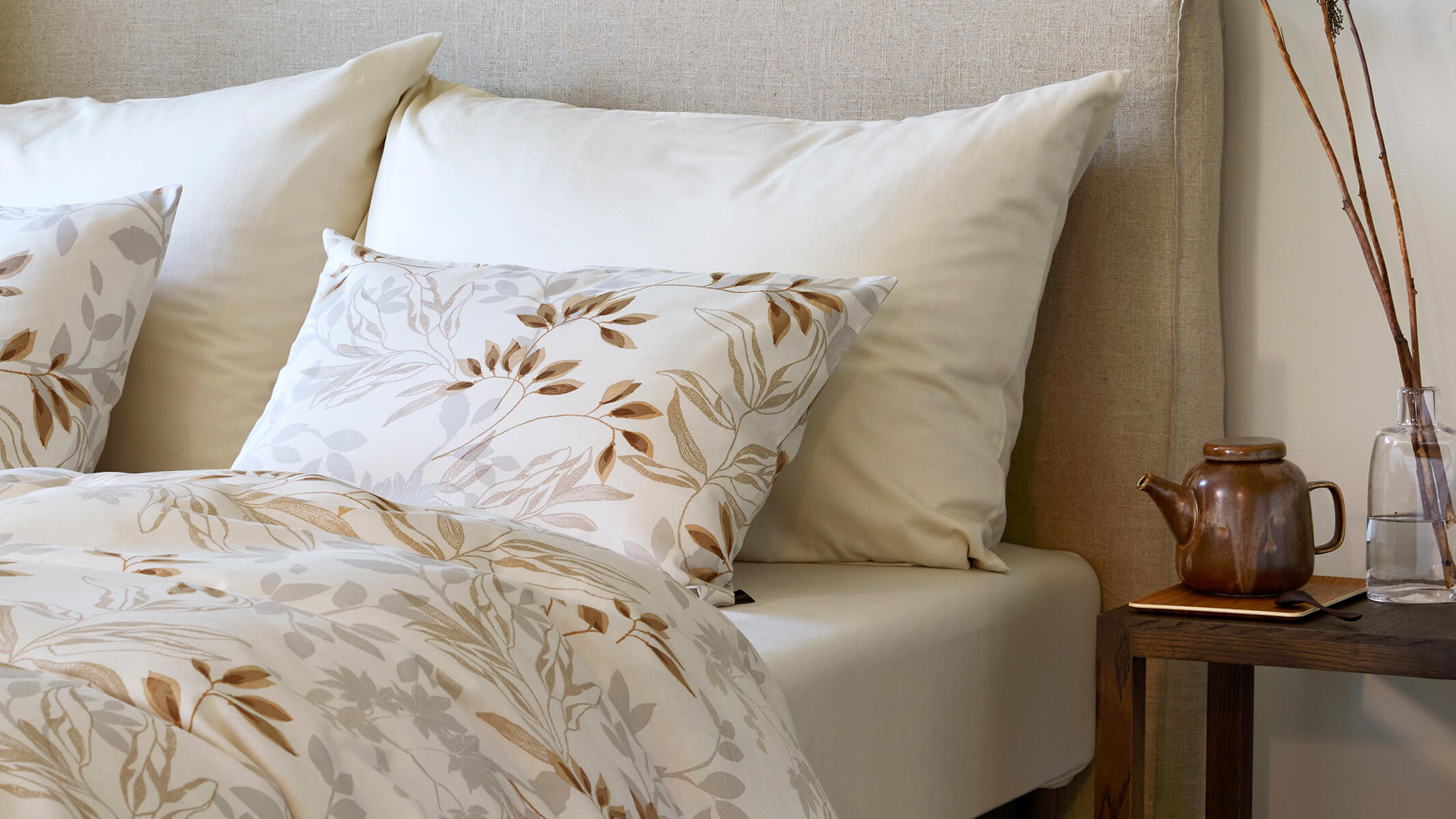 Sengetøj i beige med blomstret mønstre.