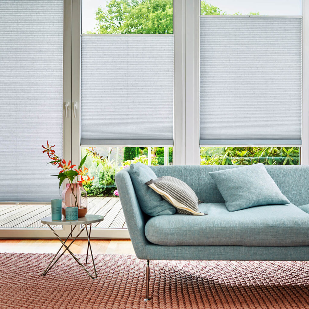 Lyse Daemp-gardiner i en stue med turkisblå sofa og rødt tæppe.